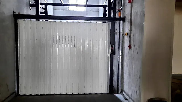 Hydraulic goods lift with a white folding shutter door in a hypermarket