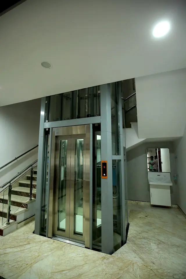 Glass home lift beside a marble staircase