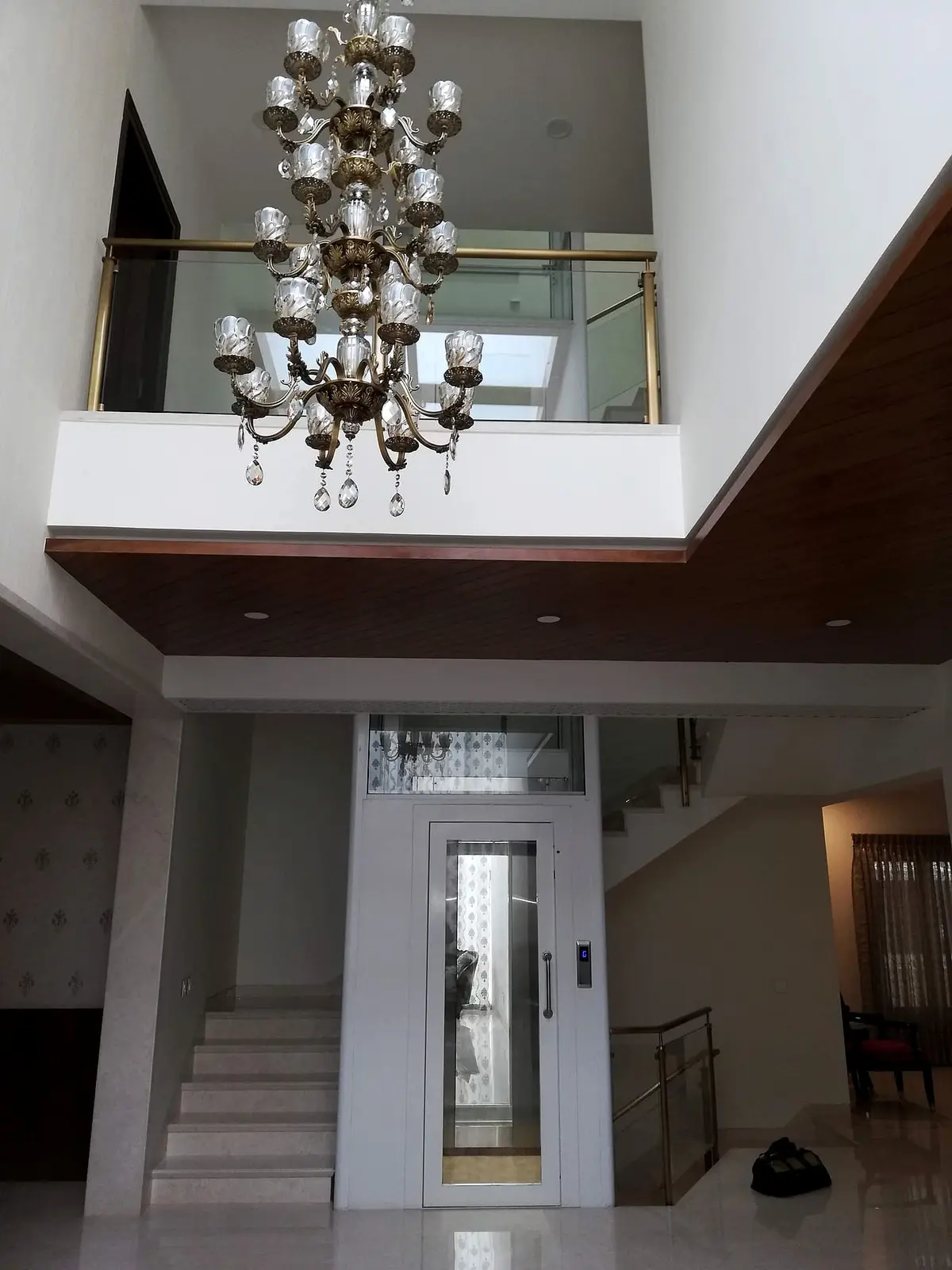 Hydraulic home lift at the foot of a staircase under a double-height chandelier