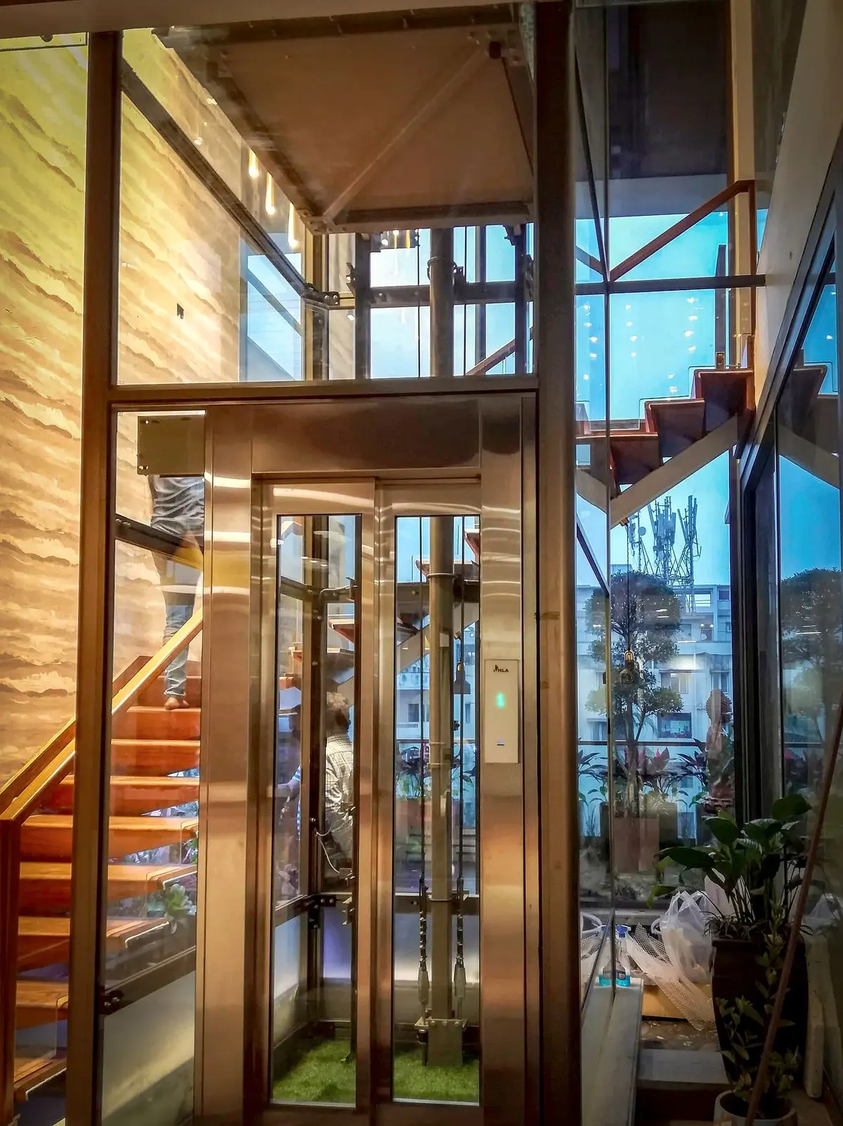Glass hydraulic home lift beside a floating wooden staircase