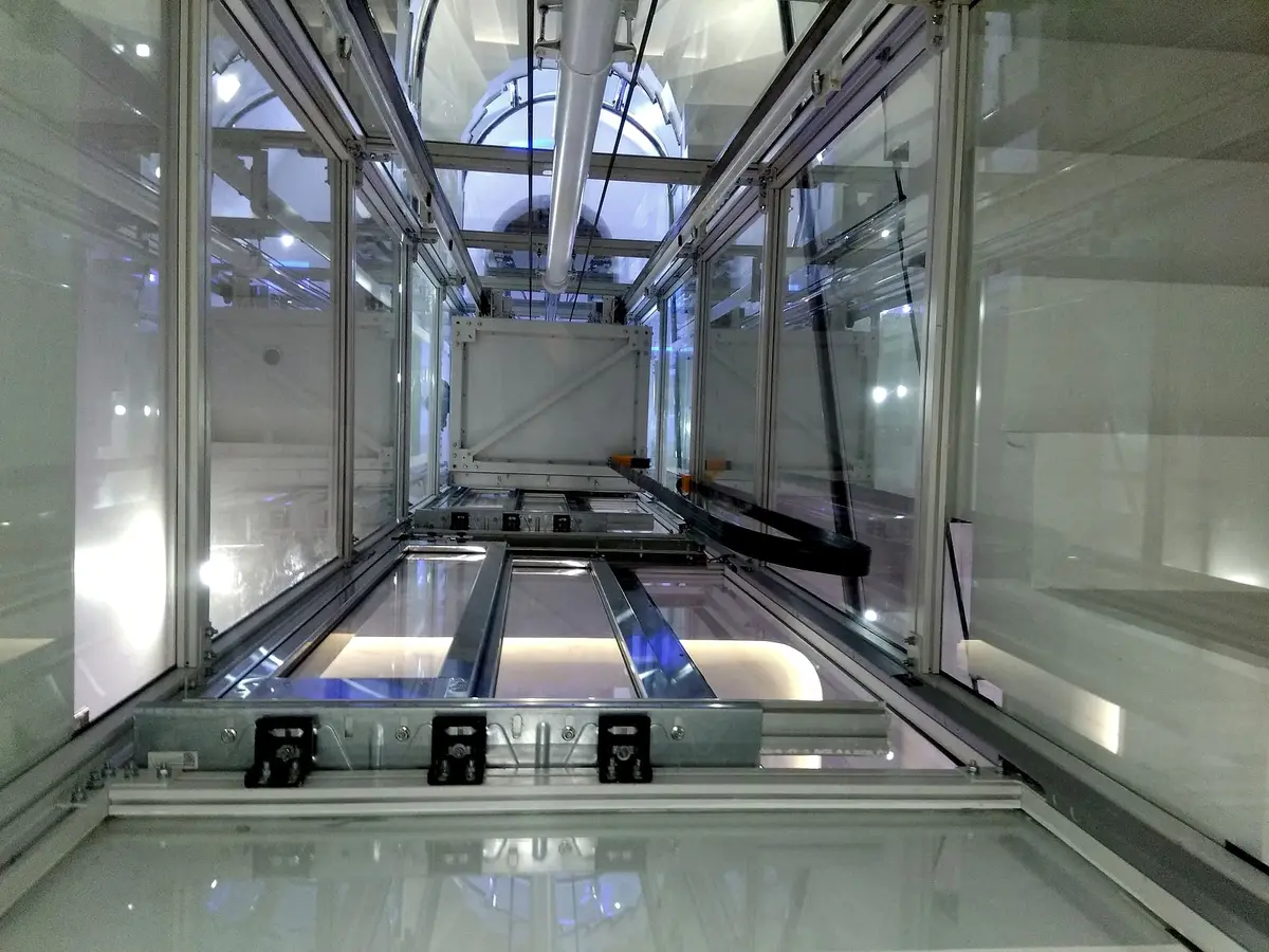 Underside of a glass lift car and its guide rails in a glass shaft